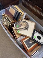 A tub containing assorted picture frames mostly stacked randomly. Frames are wood, metal, and ornate, some with photos.
