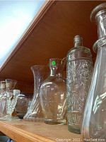 Shelf with clear etched and floral pattern decanters, a tall etched glass vase, and small bowls grouped together