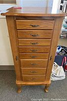 Front view of a tall wooden jewelry armoire with multiple drawers and metal handles, standing on carved legs.