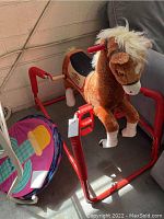 Front side view of brown plush bouncy horse on red metal frame next to colorful play tunnel