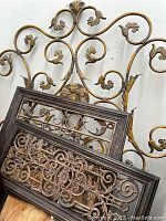 Three metal wall decor pieces including one large gold floral scroll piece and two smaller framed bronze scrollwork pieces.