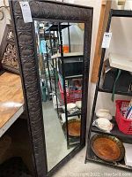 Full view of large rectangular mirror showing embossed floral and leaf patterned frame in dark bronze/brown finish.