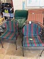 Six outdoor metal patio chairs with striped cushions, stacked closely in a storage area, showing front and side views.