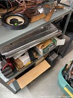 Shelf with jump starter battery, clamp tool, circular metal part, thermal insulation panel, various boxes and containers