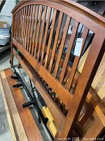 Front angled view of the queen size wooden headboard showing vertical slats and curved top rail, includes metal rods attached below.
