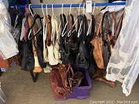Purses hanging on a clothes rack and additional purses in a purple plastic bin underneath.