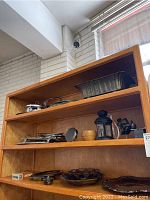 Photo shows three shelves containing various silverplate items: a round covered serving dish, a warming dish with glass insert, metal baskets, a silverplate teapot, and other assorted serveware items.