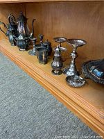 Full view of shelf showing multiple silverplate items including coffee/tea pots to left, candle holders, compote stands and serving dish to right
