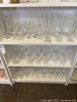 Three shelves filled with clear glassware including champagne flutes, various sizes and shapes of stemmed glasses and smaller drinking glasses.