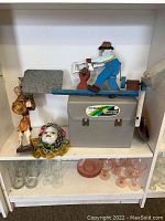 Wide view of shelf showing clear and pink stemware, Mardi Gras mask, weather vane mounted on box, and two figurines