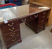 Full view of the mahogany desk with glass top showing double pedestal drawer configuration and brass handles.