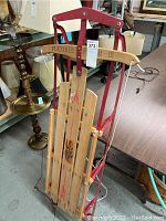 Full view of folded Flexible Flyer III toboggan with red metal frame and wooden slats, showing overall item