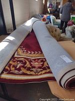 Rolled wool carpet partially unrolled on a table showing the border and floral design in red, beige, and yellow