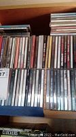Drawer filled with multiple rows of music CDs in jewel cases, two layers deep in a wooden drawer. Album titles visible include various rock and alternative music artists.