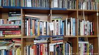 Bookshelf with assorted hardcover and paperback books tightly packed, showing multiple rows of books.
