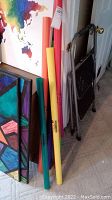 7 Boomwhacker tubes leaning against a wall next to some paintings and a step ladder.