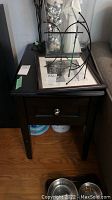 Wooden end table with drawer and lower shelf shown from front left angle, dark finish