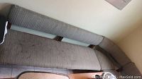 Photo of a wrap-around bench showing striped gray upholstery with visible stains and wear, angled corner seating with wooden frame visible underneath upholstery.