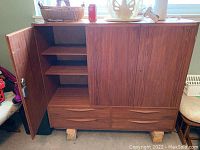Front view of Mid Century cabinet with three doors and four drawers, open door showing interior shelves.
