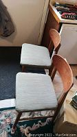 Pair of mid-century chairs with wooden frames and light upholstered seats seen from an angle, showing overall condition and style.