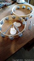 Photo showing two wooden tambourines with metal jingles, metal triangle, and white wooden tuning fork holder with tuning forks.