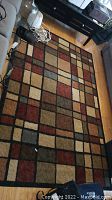 Full view of the rectangular area rug laid on wooden floor showing geometric pattern featuring squares and rectangles in earthy colors.