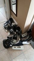 Four pairs of ice hockey skates in black and white on floor, assorted sizes, visible wear and need cleaning.