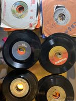 Top view of four individual 45 RPM vinyl records laid out, showing different label brands and sleeve types.