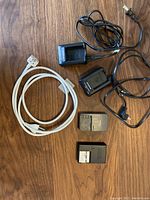 Five assorted camera battery chargers on wooden surface, including two Olympus BCS-1 chargers and power cords.