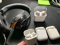Photo of 1 black Beats on-ear headphones with torn ear foam, 3 white Apple AirPods charging cases missing earbuds, and 1 white AirPod-like earbud charging case.