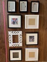 Nine assorted picture frames of various styles and sizes arranged on a wood floor beside a measuring tape for scale.
