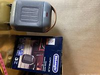 Photo showing the DeLonghi Capsule heater unit with a brown handle and the original box beside it.