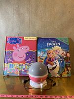 Photo showing two children's books and a starry night light on a wooden floor with a measuring tape indicating approximate sizes.