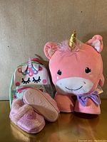 Kids unicorn backpack, large pink unicorn plush, and small pink slippers shown together