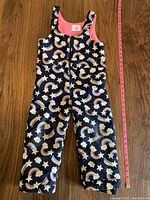 Front view of kids snow pants showing full length with rainbow and cloud patterns against navy background, pink inner lining visible at top.