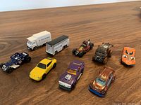 Collection of 8 assorted toy cars on wooden table including trucks, vintage cars, and race cars taken from a top angle
