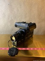 Front and left side view of the Canon AV-260 vintage video camera showing lens, viewfinder and camera body with the lens cap placed on the table.