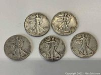 Front of five Walking Liberty half dollar coins showing Lady Liberty walking and inscriptions 'IN GOD WE TRUST' and dates ranging from 1917 to 1943.