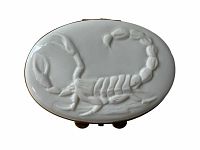 Top view of white oval porcelain box with a detailed scorpion relief on the lid.