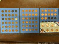 Three blue coin album pages displaying over 70 Lincoln pennies from 1929 and forward, including wheat pennies and memorial pennies. Coins arranged in circular slots with some empty slots.