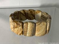 Jasper stone bracelet placed on a reflective surface showing rectangular polished jasper beads with natural earthy Brown and tan color patterns.