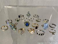 Overview of all 19 vintage costume jewelry rings with various colored stones and bands arranged in a display case.