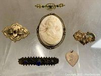 Overview of six Victorian costume jewelry pieces on a transparent surface, showing variety in style, materials and design.