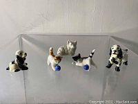 Five miniature ceramic animal figurines including cats and dogs arranged on clear surface, view from front.