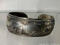 Front side view of silver cuff bracelet showing dragon engraving and textured background.