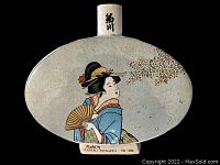 Front view of vintage oval-shaped Japanese sake decanter with a colorful illustration of a geisha holding a fan beside floral motifs and Japanese characters on the neck.