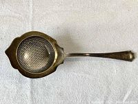 Full top view of the sterling silver tea strainer laid flat showing perforated bowl and handle.