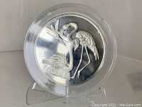Front side of medallion showing two Greater Flamingos standing by a branch, highly detailed raised design.
