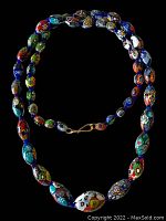 Close-up photo of the full necklace laid out in a circle on a black background showing colorful multi-patterned Millefiori Murano glass beads hand-crafted with floral designs and metal clasp.
