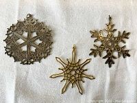 Three vintage Museum of Modern Art snowflake metal ornaments displayed flat on fabric background showing all three designs.